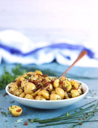 Authentic German Potato Salad in a white bowl with a copper spoon on a blue background