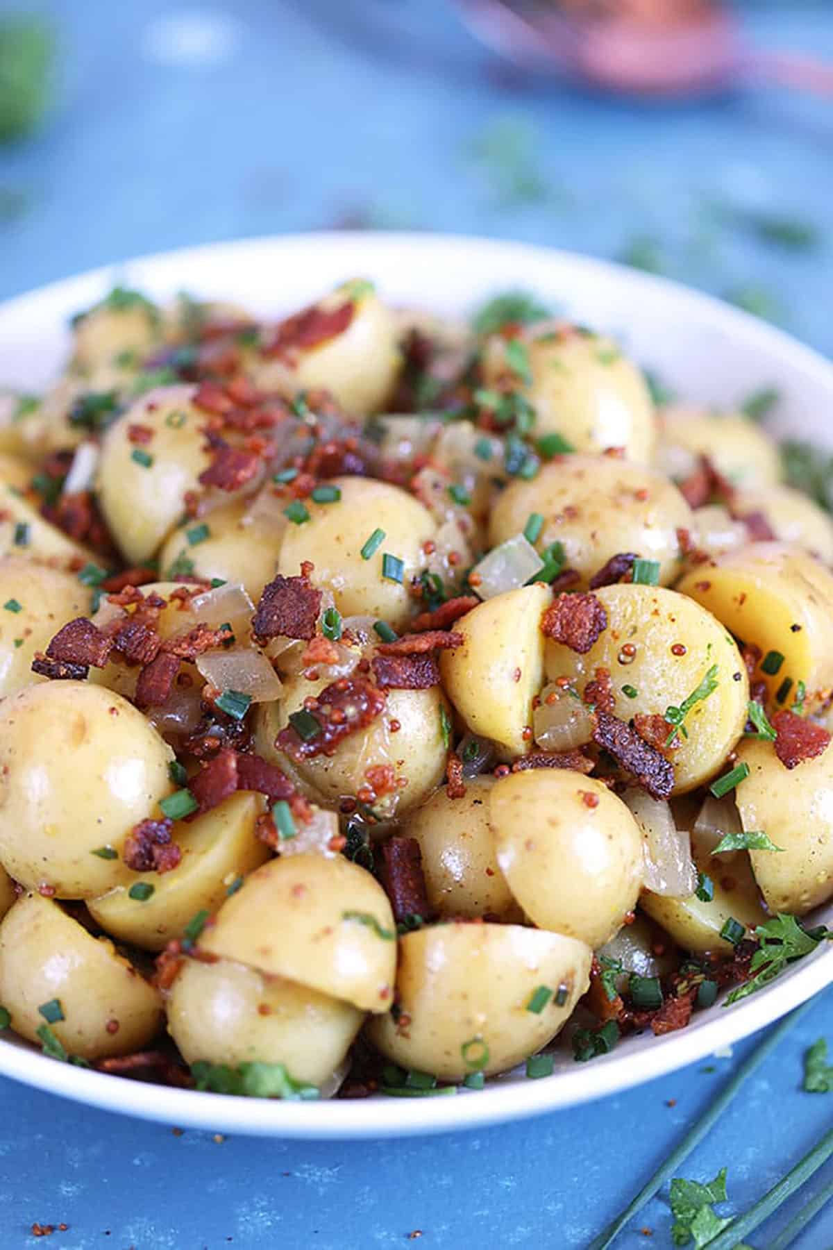 German Potato Salad with bacon in a white bowl on a blue background 