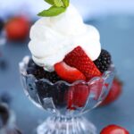 Bowl full of berries with homemade whipped cream and a mint leaf on top