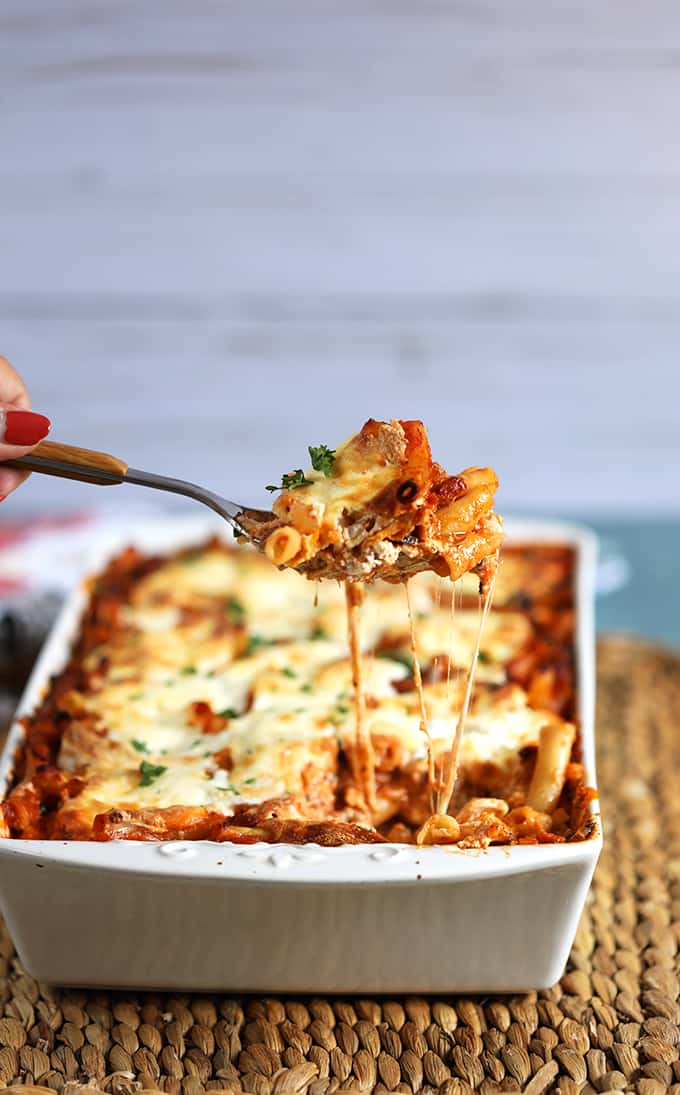 The Very Best Baked Ziti recipe in a white baking dish with a spoonful being scooped out and stretchy melty cheese from thesuburbansoapbox.com