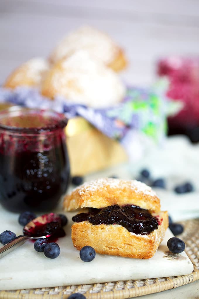 Blueberry jam on a biscuit with a jar of blueberry jam in the background on a white marble board from TheSuburbanSoapbox.com