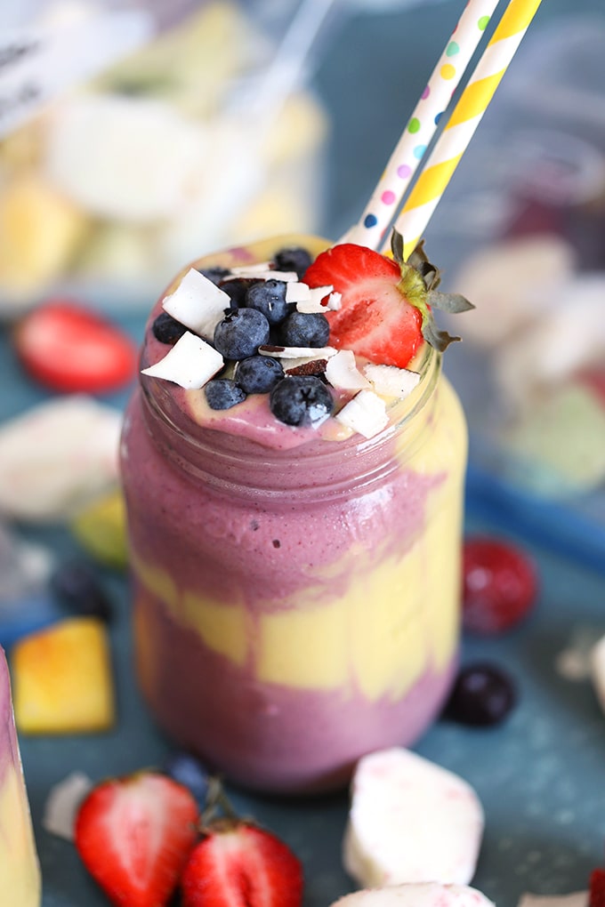 Layered smoothie with fresh fruit on top and paper straws on a blue background from TheSuburbansoapbox.com