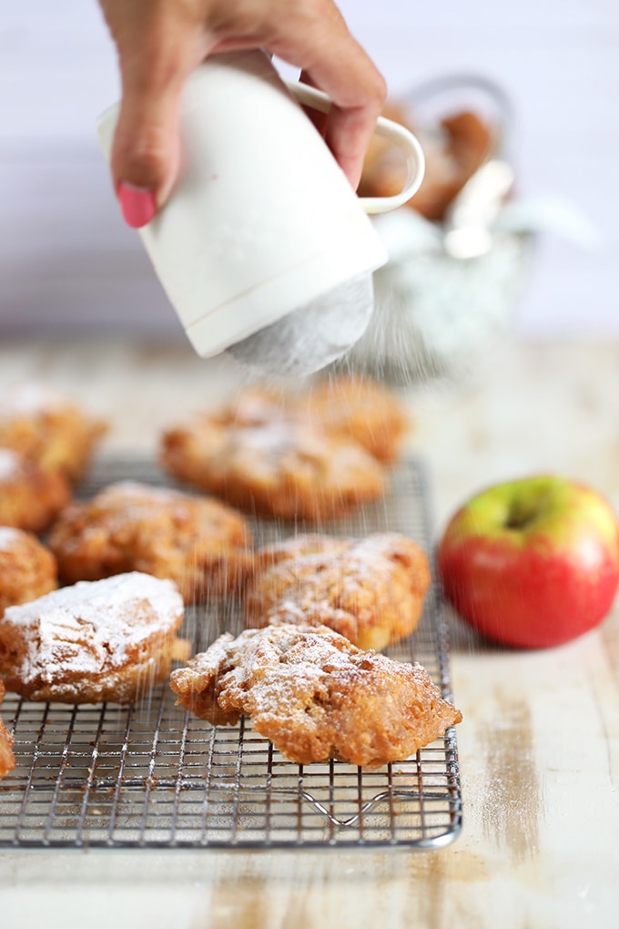 Apple fritters on a cooling rack with powdered sugar being dusted on top.