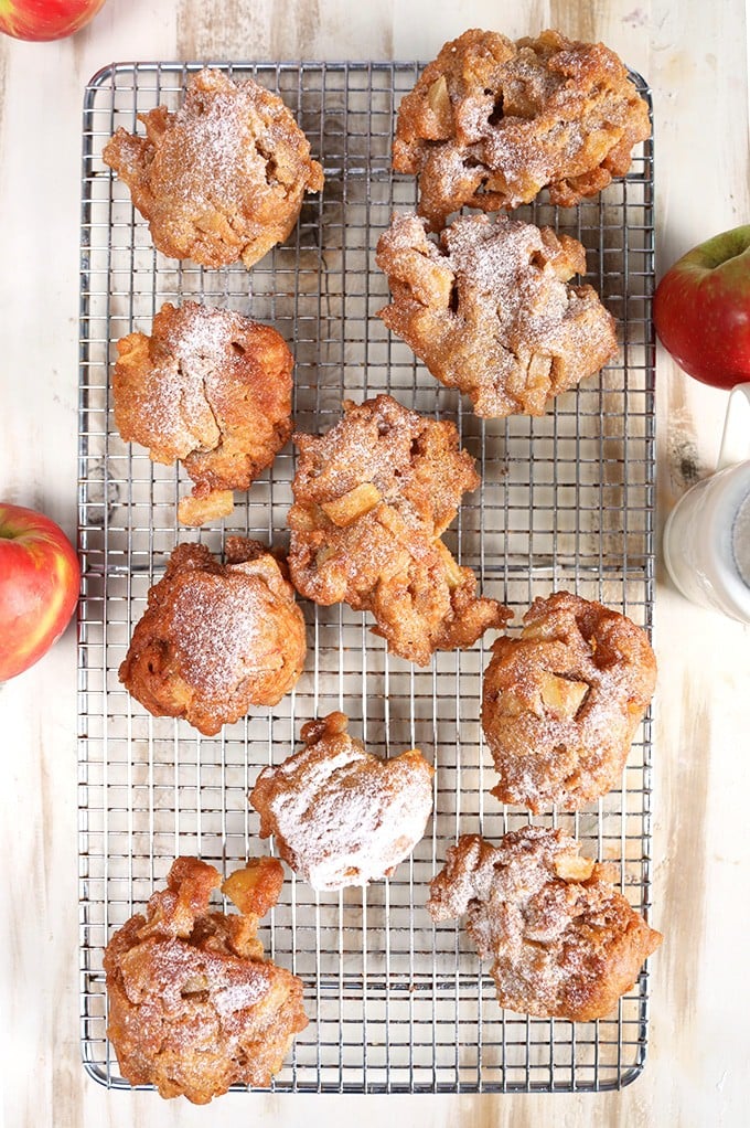 Apple fritters on a cooling rack on a rustic white background with apples from TheSuburbanSoapbox.com
