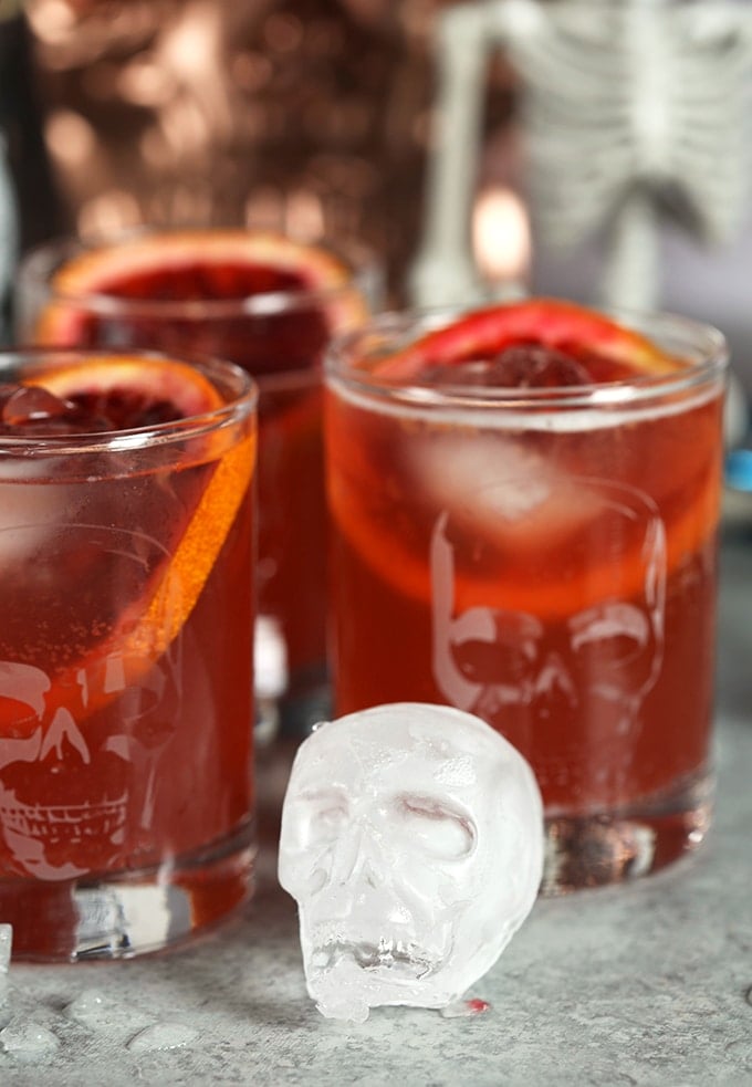 Skull ice cube in front of three highball glasses filled with Dark and Stormy cocktails.