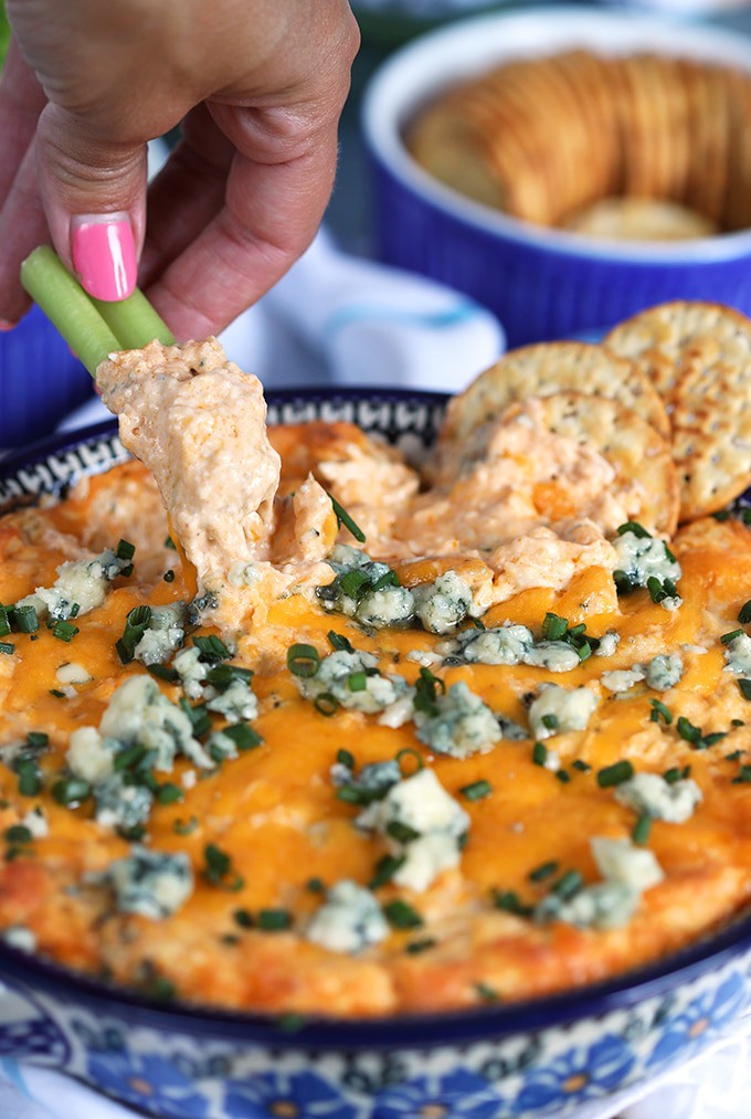 Close up shot of buffalo chicken dip with a celery stick dipping into the dish. 