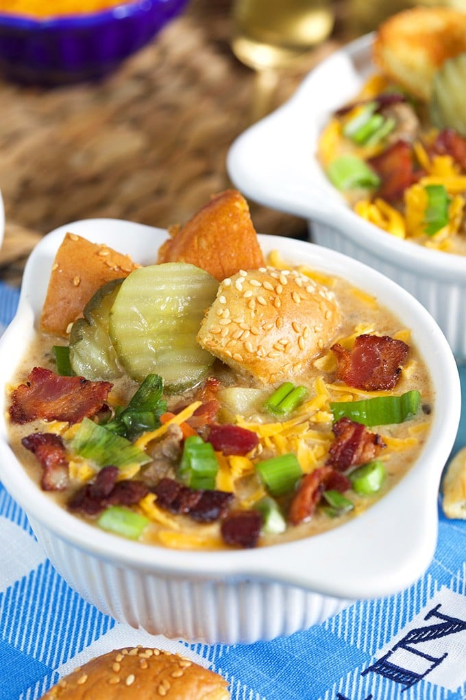 Close up shot of Bacon Cheeseburger Soup in a white bowl with pickles burger bun croutons, bacon and cheese.