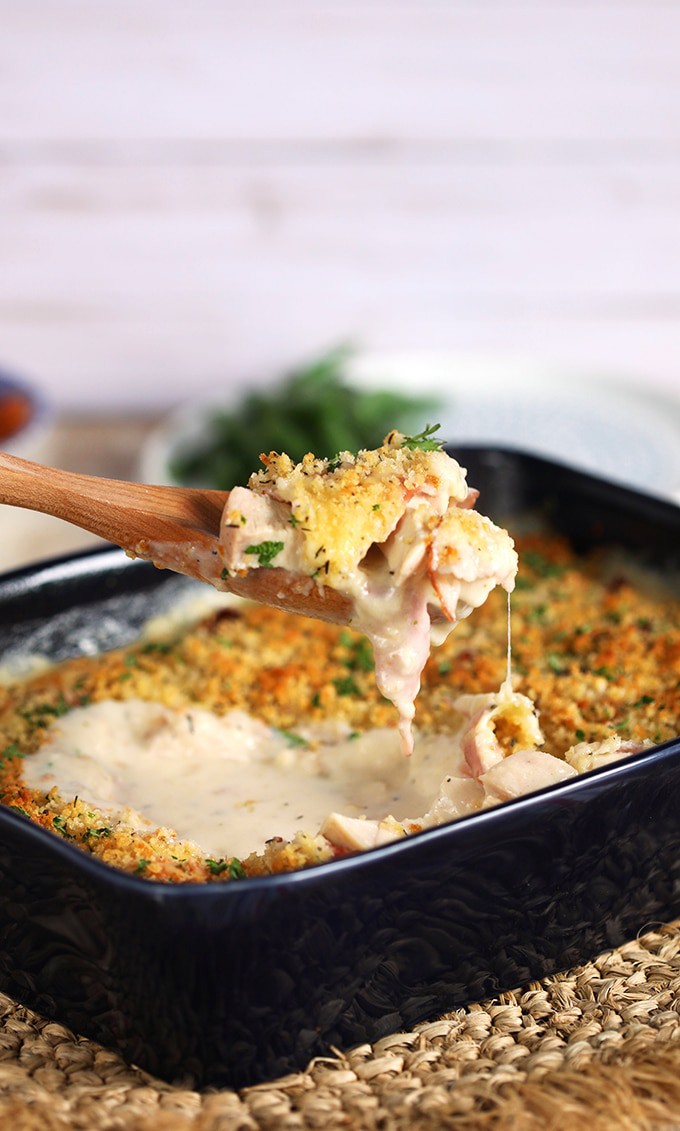 Chicken Cordon Bleu Casserole in a blue baking dish with a spoon serving it.