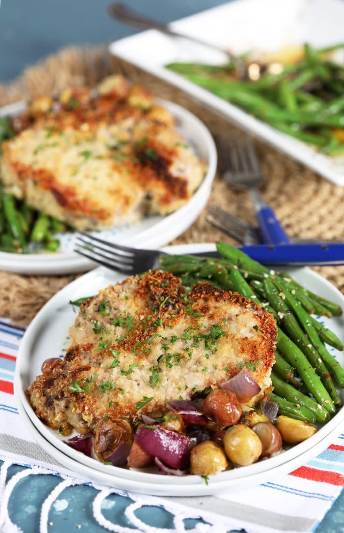 Crispy Parmesan Crusted Baked Pork Chops with green beans on a white plate on a blue background.