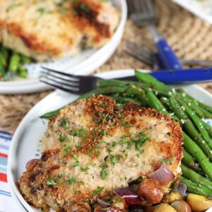 Parmesan Crusted Baked Pork Chops with green beans and potatoes on a white plate with a blue fork.