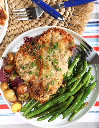 Overhead shot of Parmesan Crusted Baked Pork Chops with green beans and potatoes on a white plate.