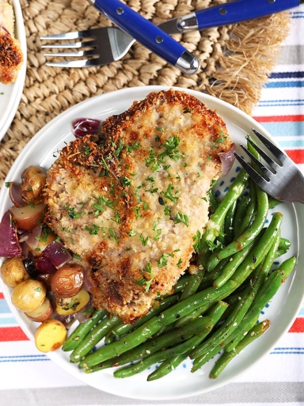 Overhead shot of Parmesan Crusted Baked Pork Chops with green beans and potatoes on a white plate.