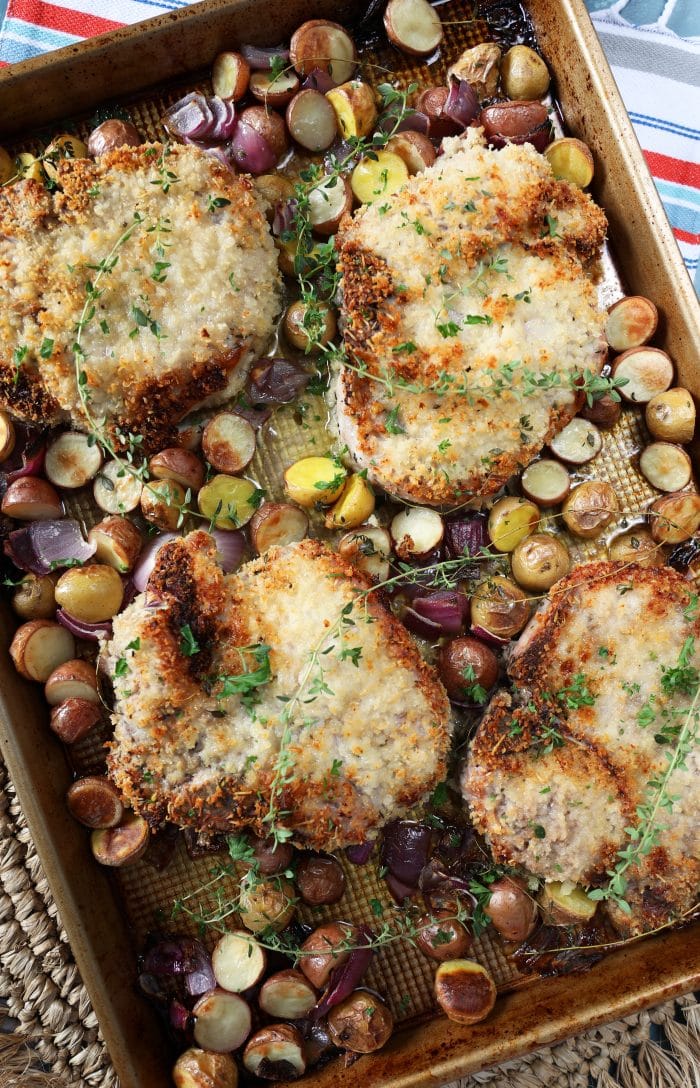 Overhead shot of cooked Parmesan Crusted Baked Pork Chops with potatoes and onions on a striped placemat.