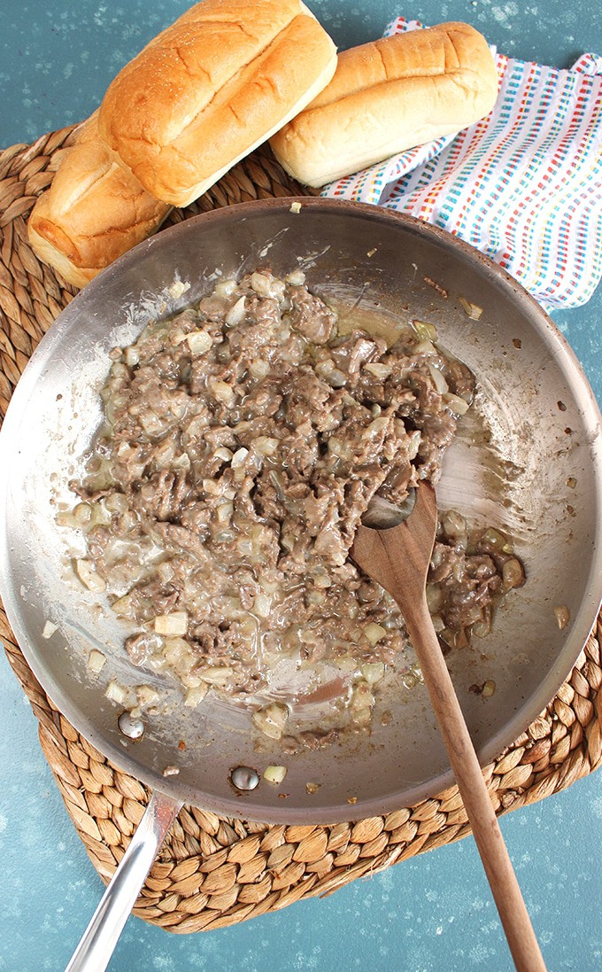 Philly cheesesteak in a skillet with rolls on the side for sandwiches.
