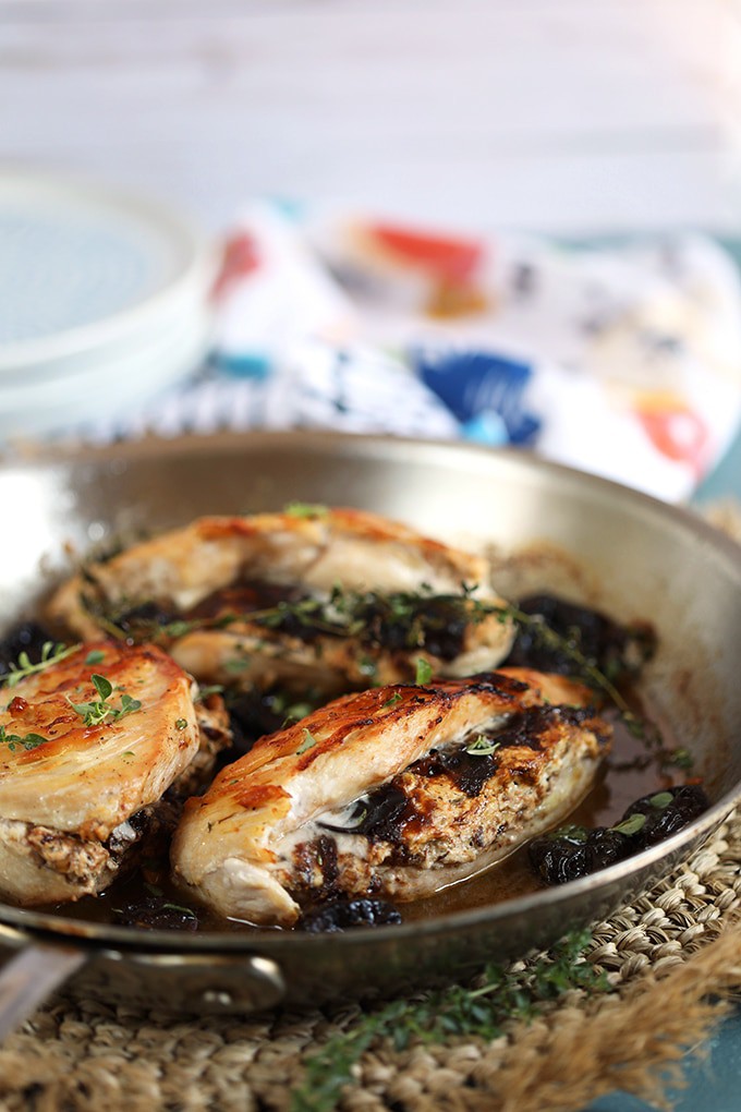Three stuffed chicken breasts in a skillet with prune sauce.