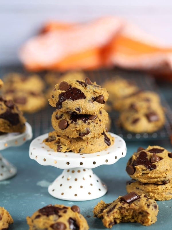 Three pumpkin chocolate chip cookies on a white cupcake stand.