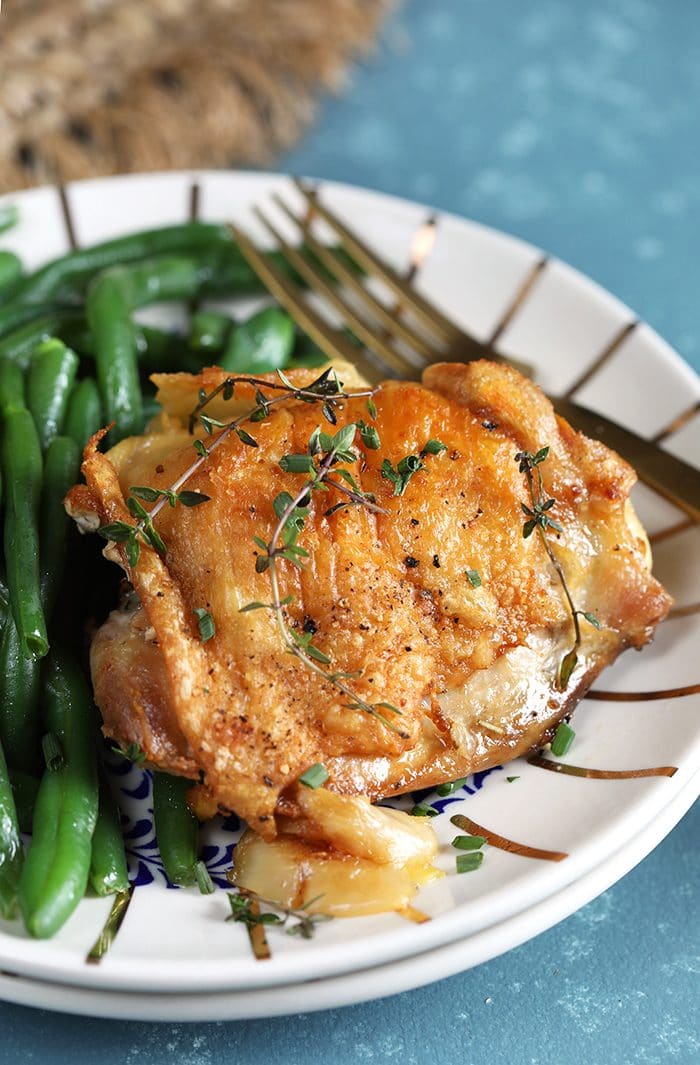 Crispy Baked Chicken Thighs with Garlic Herb Sauce on a white plate with green beans.