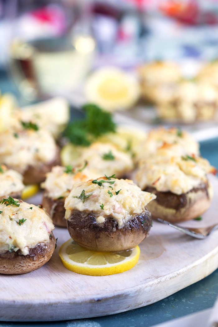 Crab stuffed mushrooms on a white board with lemons.