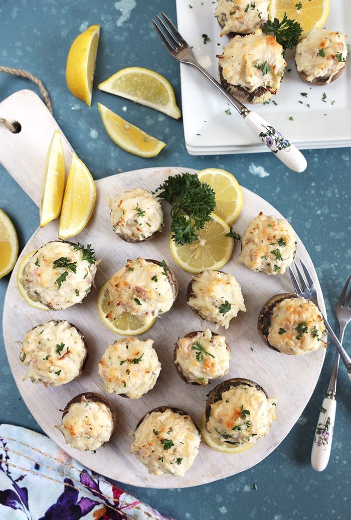Overhead shot of crab stuffed mushrooms on a white board with lemons and parsley.