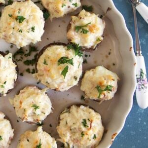 Crab Stuffed Mushrooms in a baking dish with lemons on a blue background.