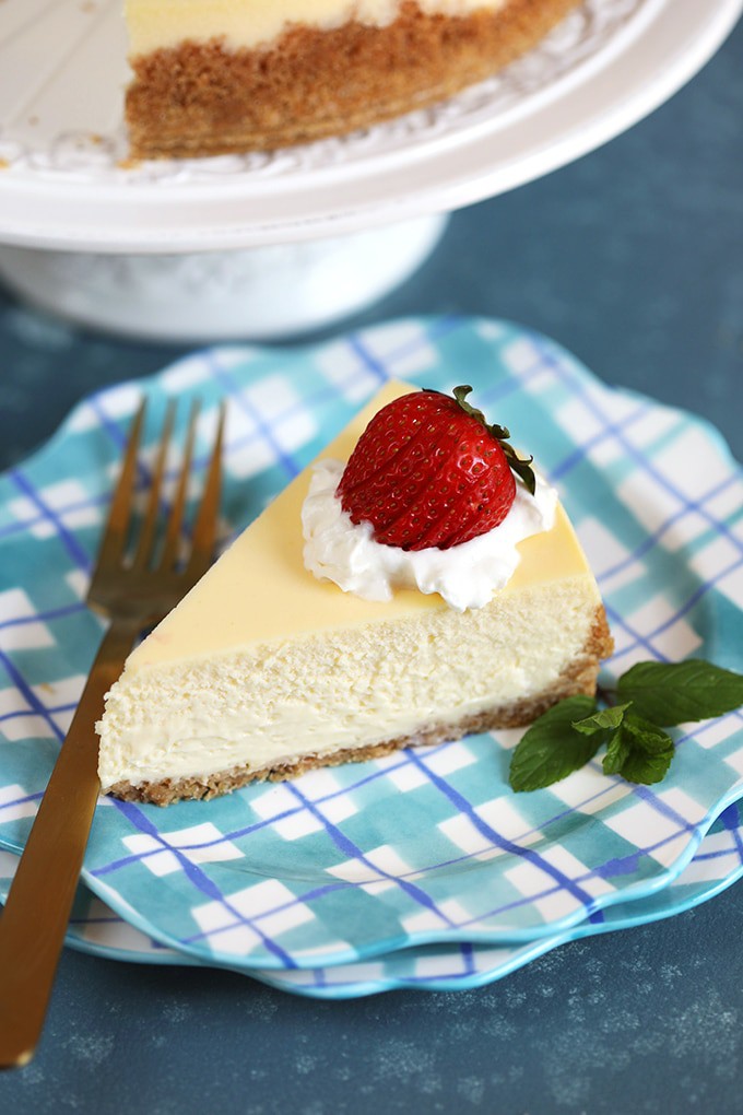 Slice of New York Cheesecake on a blue plaid plate with a gold fork.