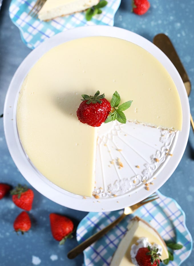 overhead shot of New York cheesecake with a slice cut out on a white cake plate with a strawberry in the center. 