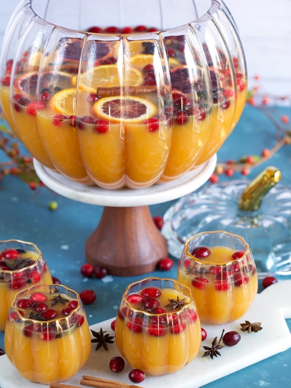 Spiced Pumpkin Punch in a glass pumpkin punch bowl with glasses of punch around on a blue background.
