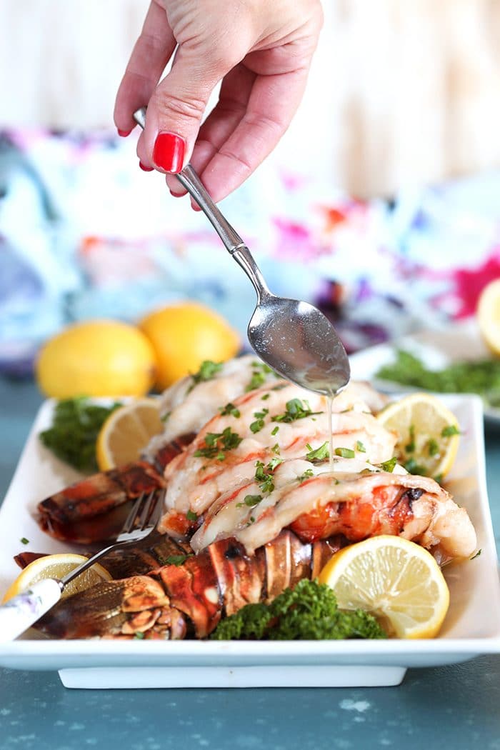 Lobster Tails on a white platter with a silver spoon drizzling melted butter over top.
