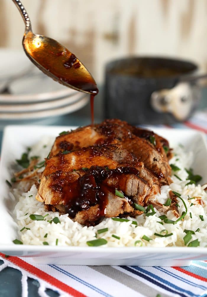 Honey garlic sauce being drizzled over Slow Cooker Pork Loin Roast on a bed of white rice.