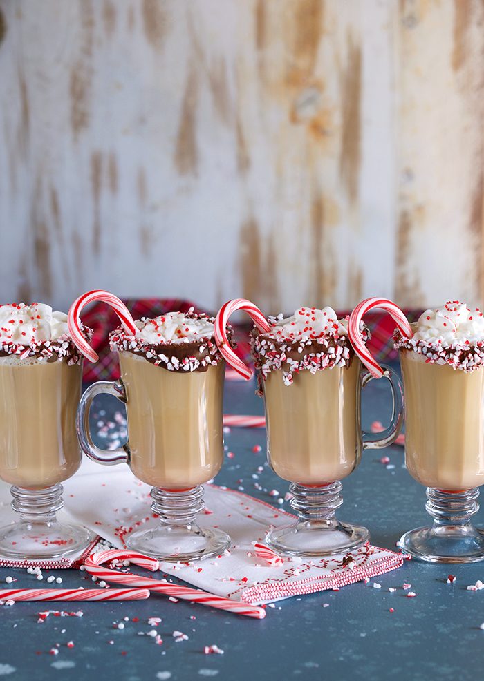 A row of Spiked Peppermint Mocha coffees in a glass mug on a blue background with candy canes and sprinkles.