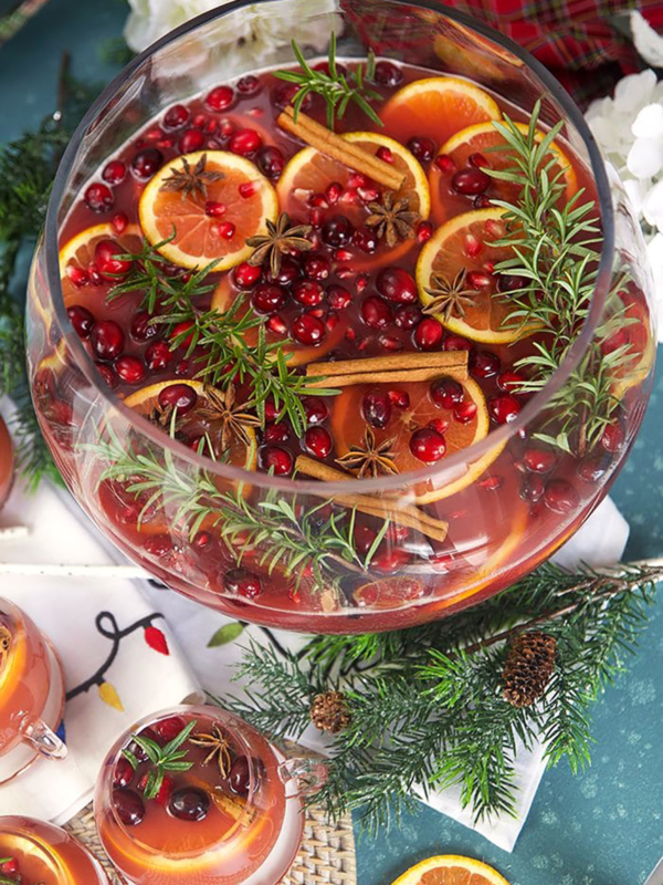 Sparkling Pomegranate Rum Punch in a glass punch bowl with rosemary sprigs and orange slices.