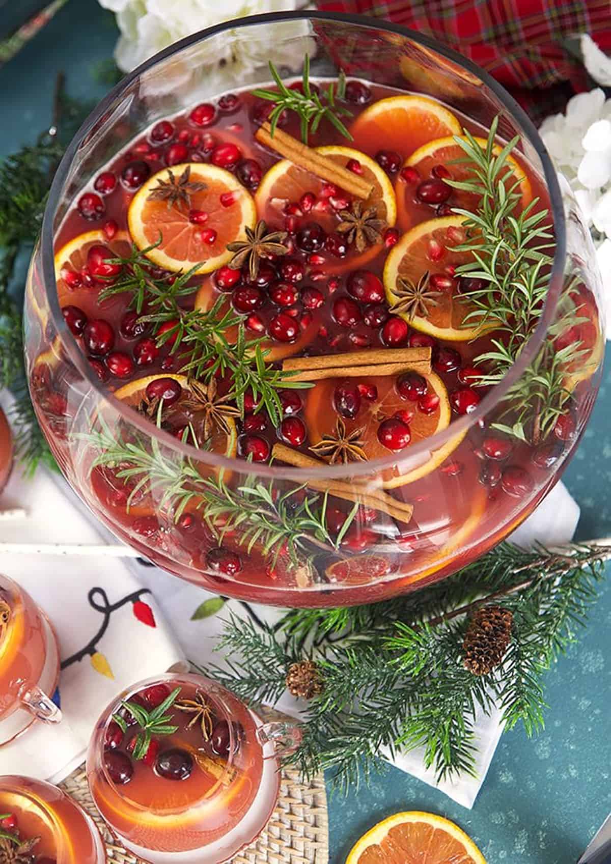Sparkling Pomegranate Rum Punch in a glass punch bowl with rosemary sprigs and orange slices. 