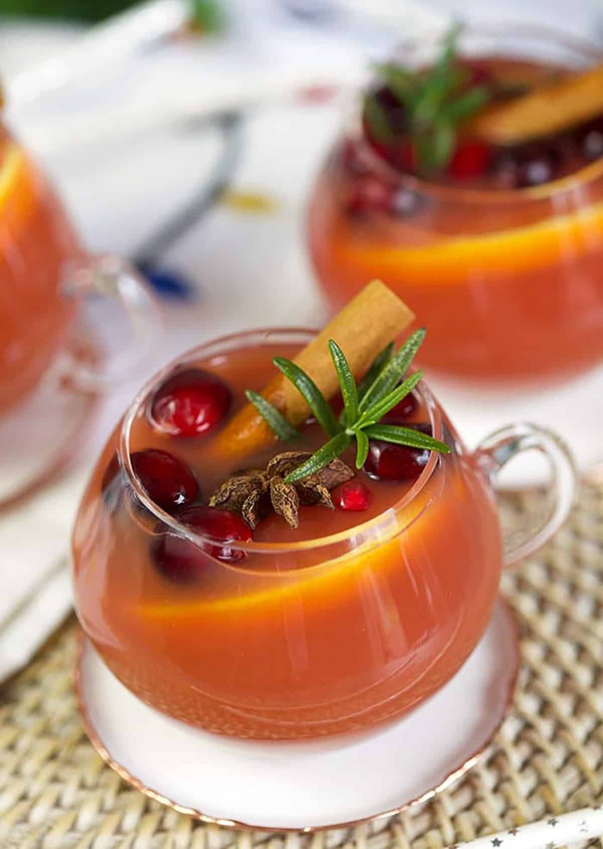 Close up shot of sparkling pomegranate rum punch in a glass with cinnamon stick and rosemary.