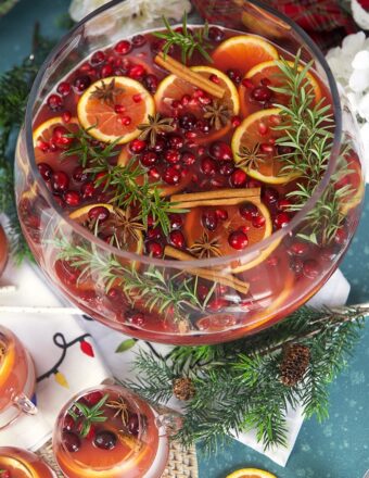 Sparkling Pomegranate Rum Punch in a glass punch bowl with rosemary sprigs and orange slices.