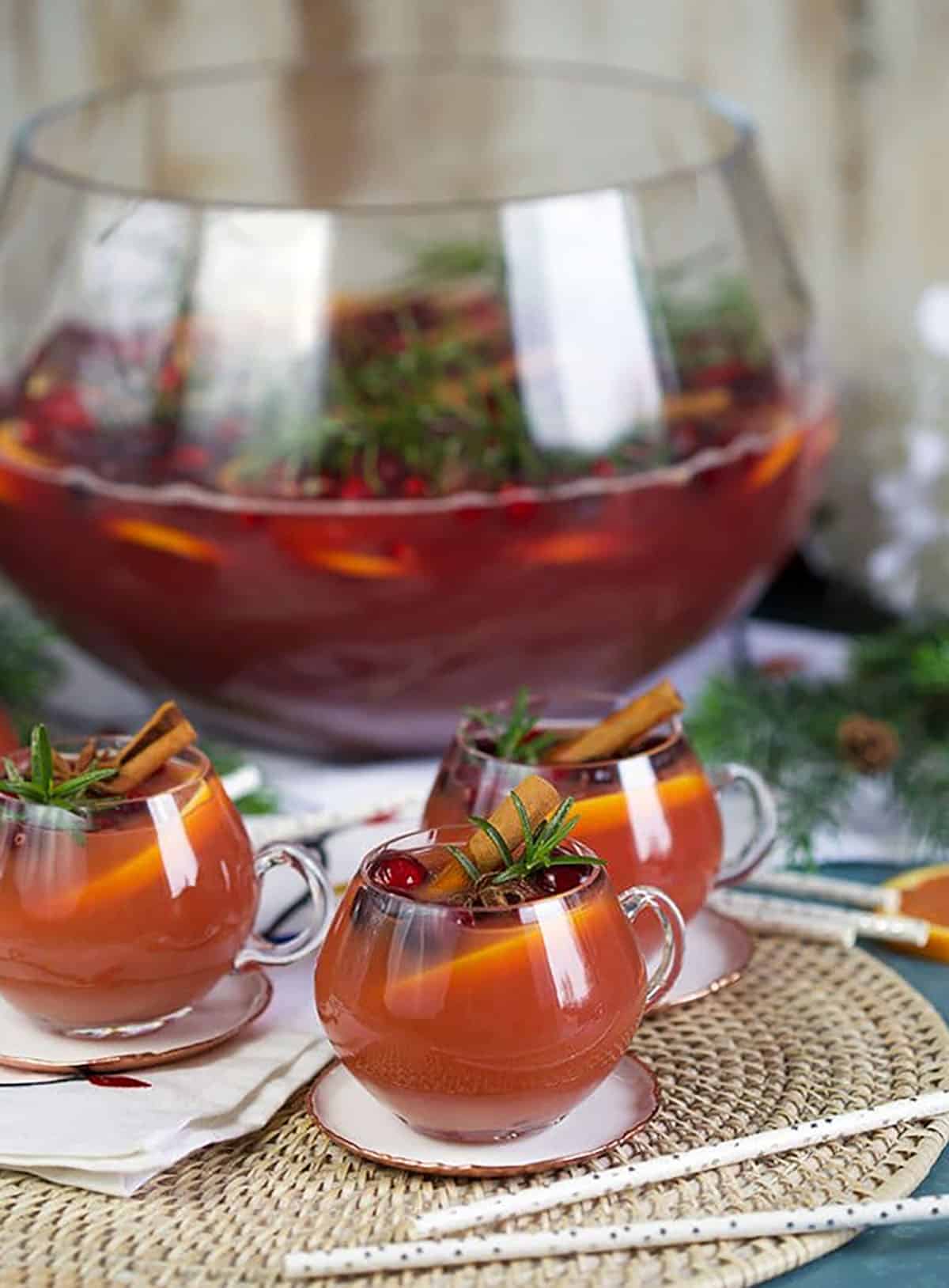 Three glasses sparkling pomegranate rum punch with cranberry, rosemary and orange slices.