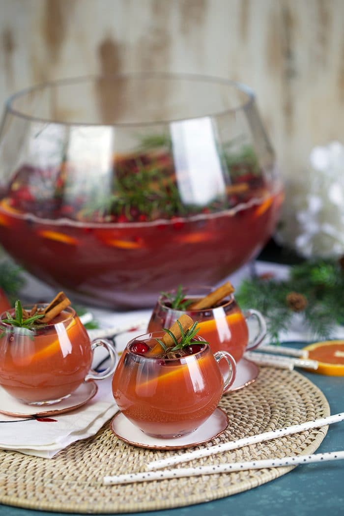 Three glasses sparkling pomegranate rum punch with cranberry, rosemary and orange slices.