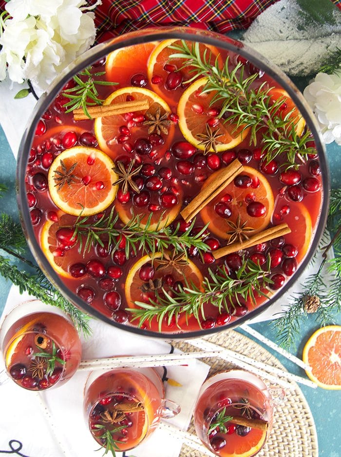 Overhead shot of sparkling pomegranate rum punch with orange slices rosemary cranberries and white napkin under neath.