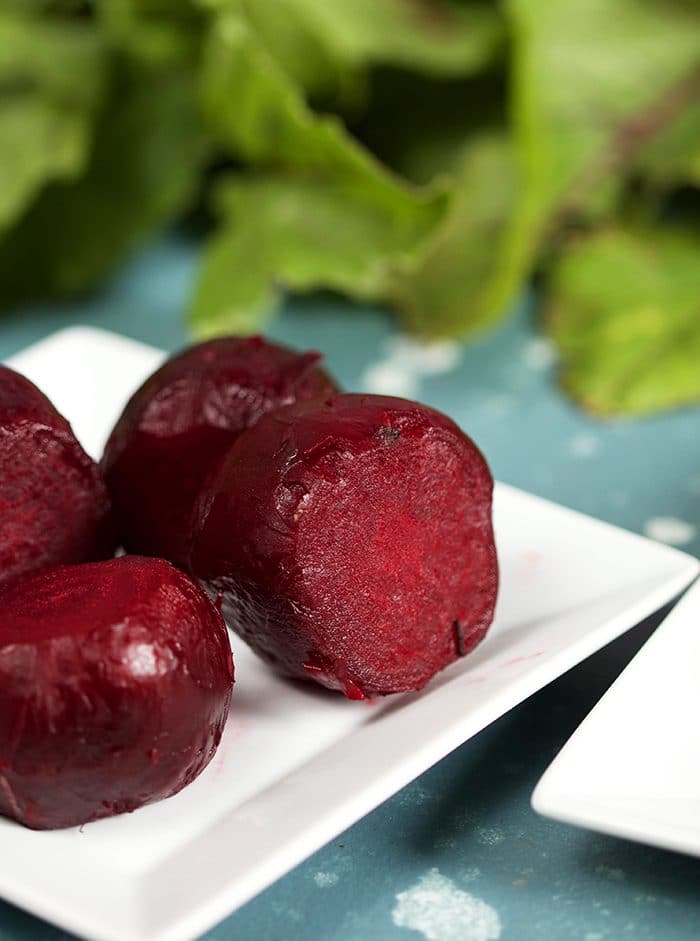 Oven Roasted Beets on a white square plate with beet greens in the background.
