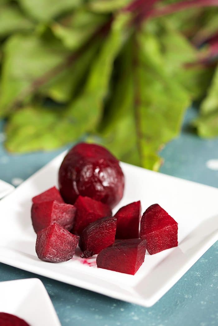 Diced Roasted Beets on a white square plate with beet greens in the background.