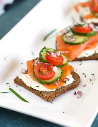 Smoked Salmon on a slice of pumpernickel with cream cheese and chives on a white platter.