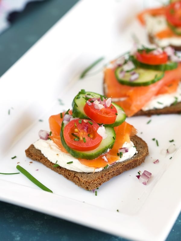 Smoked Salmon on a slice of pumpernickel with cream cheese and chives on a white platter.
