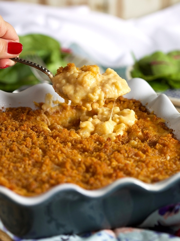 Baked Cauliflower Mac and Cheese in a blue baking dish with a crispy top and a spoonful being held above it.