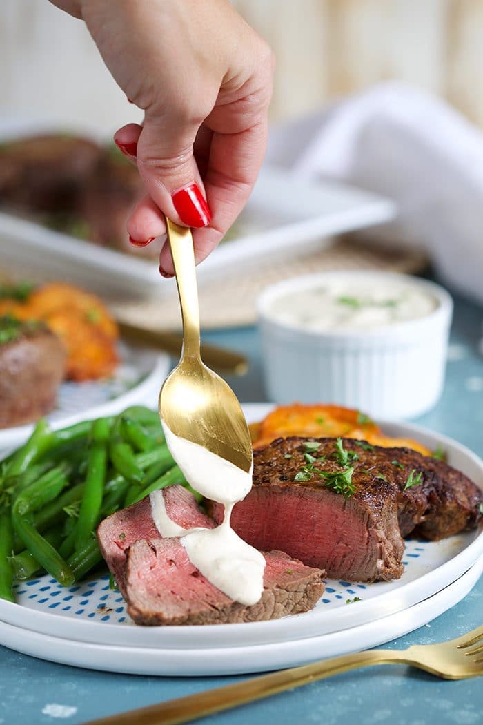 Gold spoonful of horseradish sauce being spooned over beef tenderloin on a white plate.