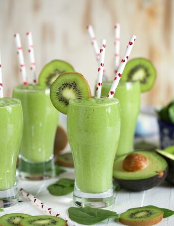 Kiwi Pineapple Spinach Smoothies with avocado half and straws with hearts on them.