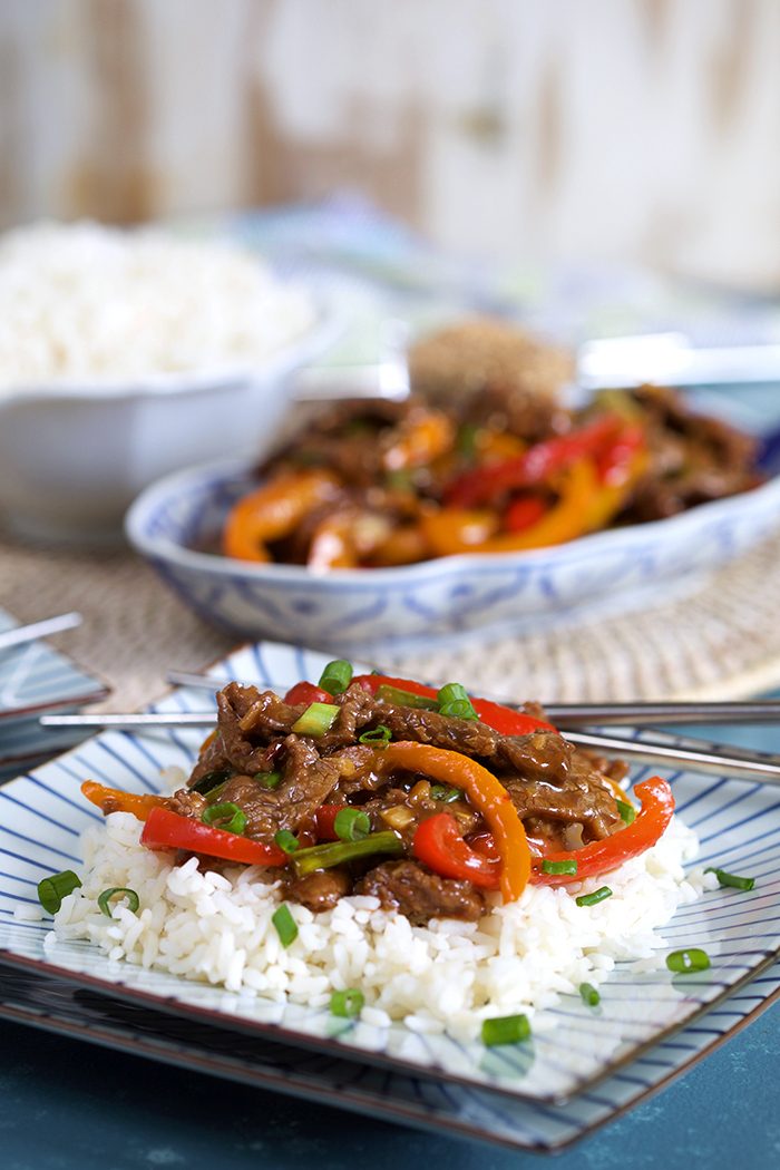 Mongolian Beef Stir Fry on a bed of white rice on a square blue and white plate with silver chopsticks.