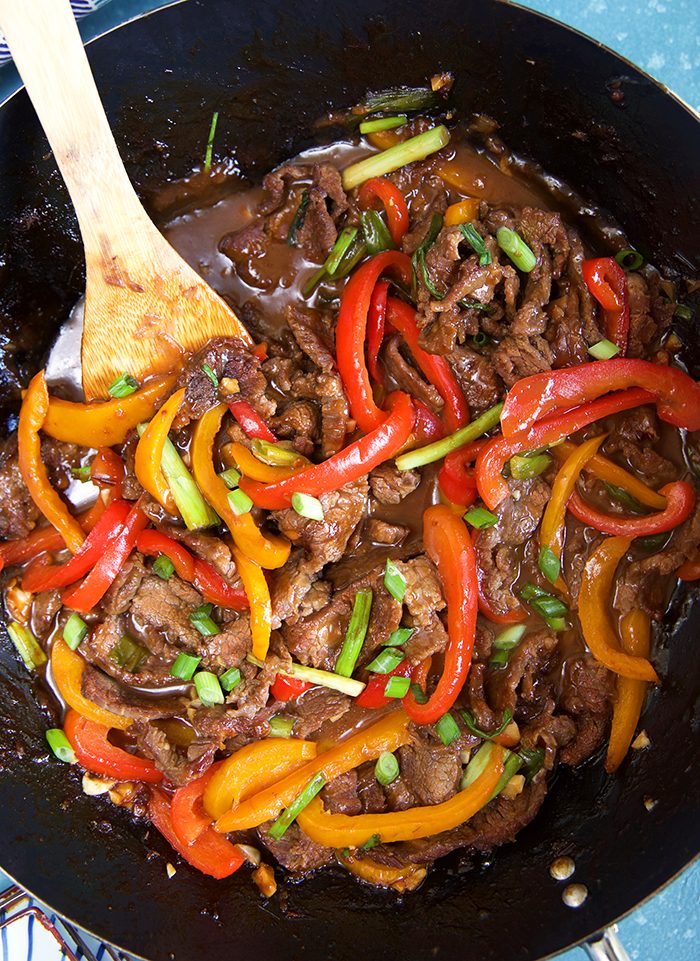 Overhead shot of Mongolian Beef in a black wok with a wooden spatula.