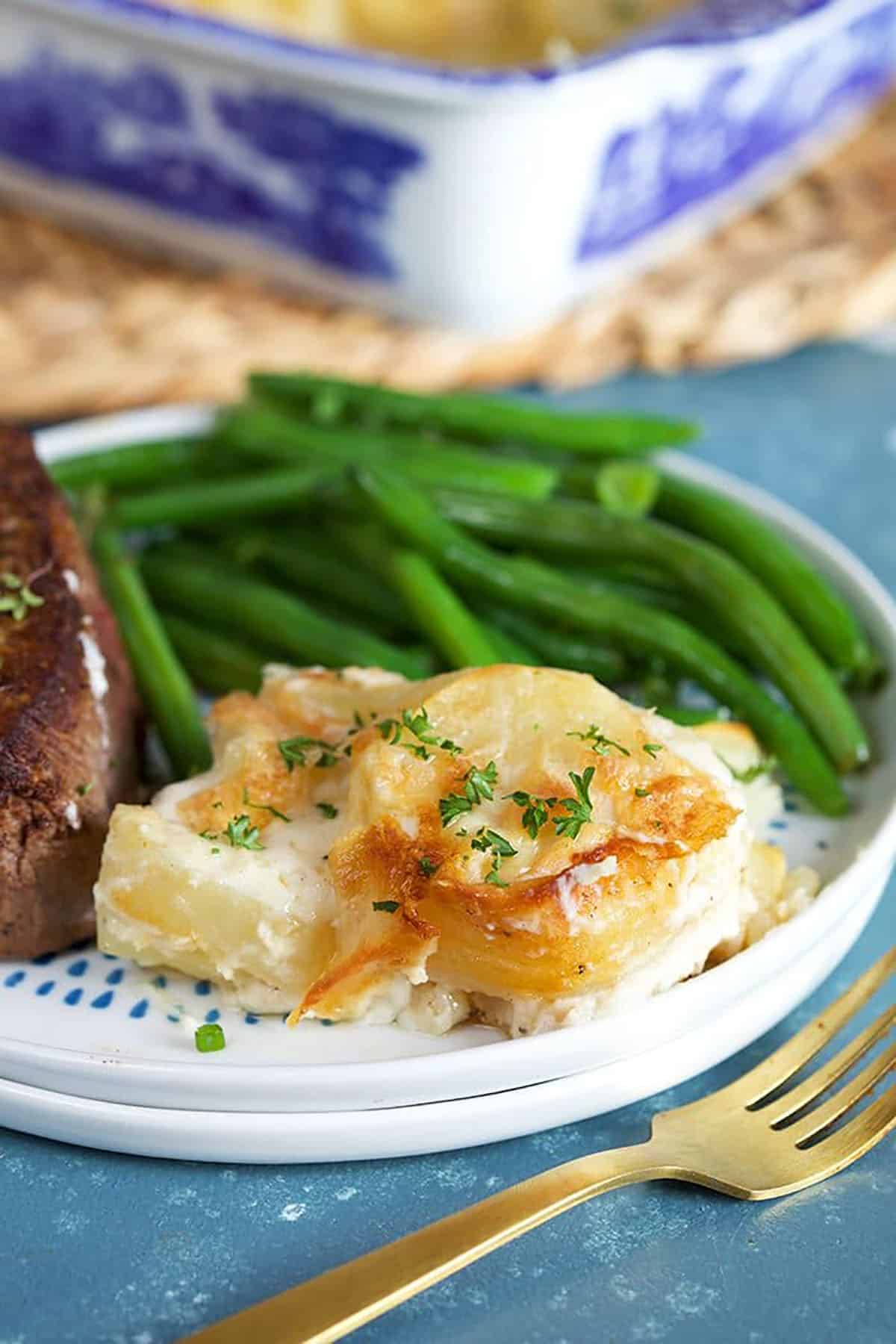 Easy Scalloped Potatoes on a white plate with green beans and filet mignon.