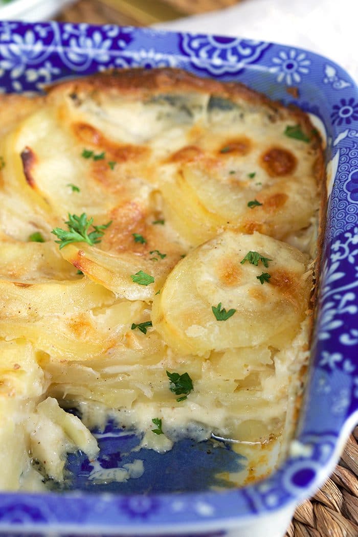 Close up of homemade scalloped potatoes in a blue and white baking dish with a square cut out to show the creamy layers of potatoes with a crispy golden crust.