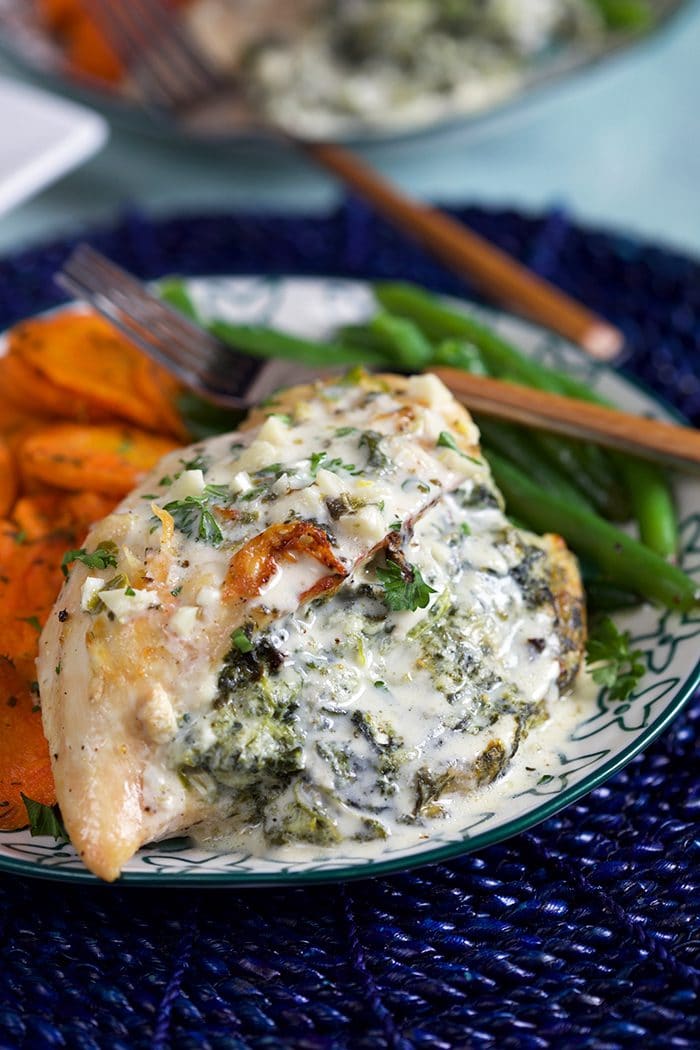 Close up of Cheesy Spinach Stuffed Chicken Breast on a plate with green beans and roasted carrot slices.