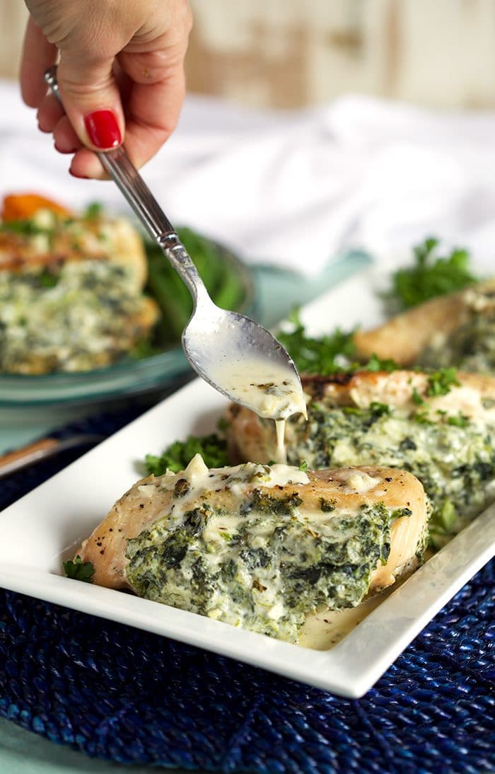 Spinach and cheese stuffed chicken breasts with a spoonful of garlic parmesan sauce drizzled overtop.